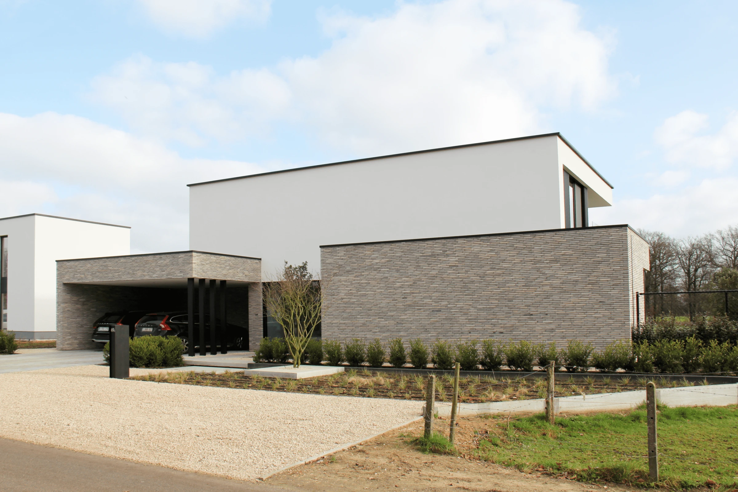 Architectuurfotografie van een modern kubistische villa met strak wit bovenvolume en een sokkel van langgerekte lichte gevelsteen.