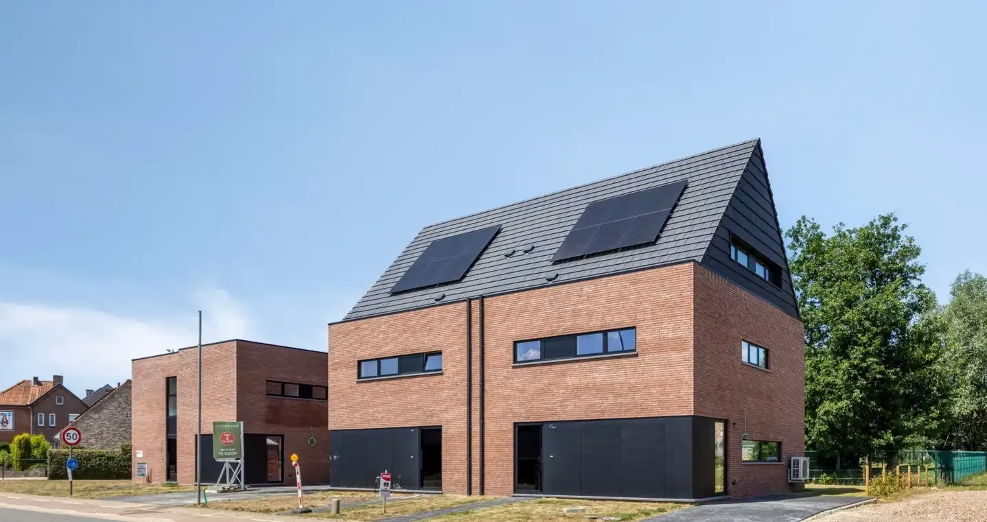 Voorgevel van drie moderne geschakelde nieuwbouw woningen in Oudsbergen, gekenmerkt door rode gevelsteen, strakke zwarte gevelbekleding en een hellend dak met geïntegreerde zonnepanelen.